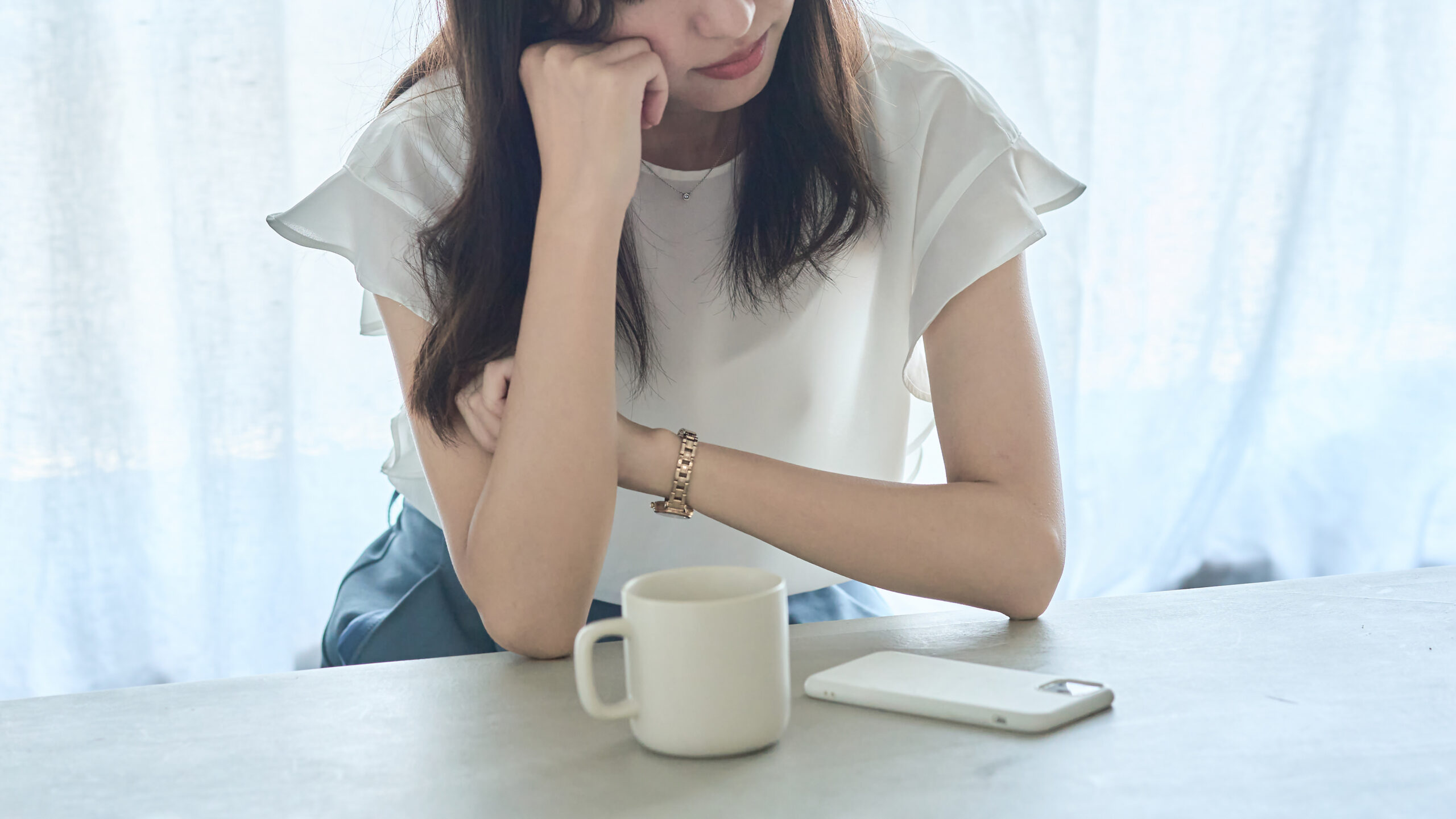 机に肘をついて考え込む長髪の女性